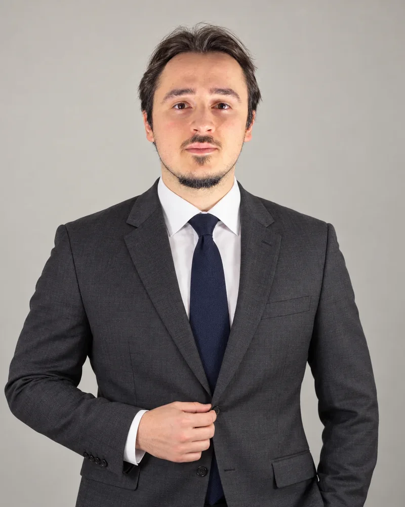 Koyu gri takım elbise ve lacivert kravatla, ceketini ilikliyor